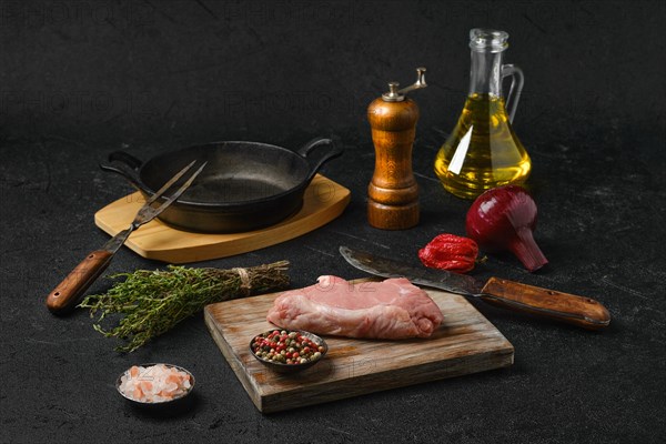 Raw veal steak bone in with ingredients for cooking on black background