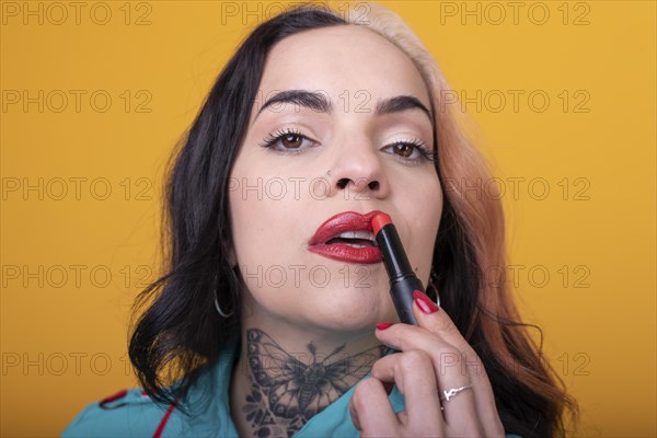 Beautiful caucasian woman applying a bright red color lipstick on her lips over yellow background