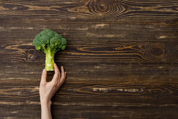 Overhead view of fresh broccoli in hands over wooden background
