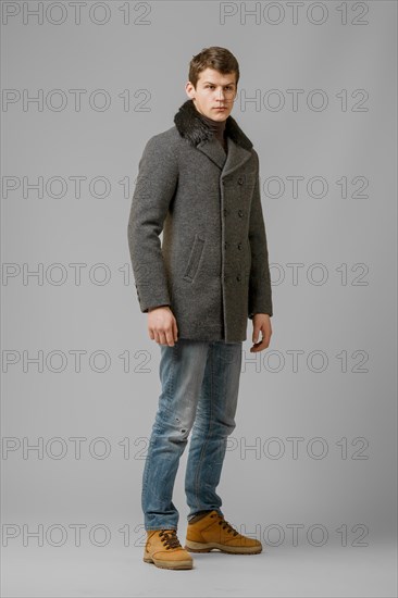 Full length portrait of handsome man in warm woolen coat posing in studio