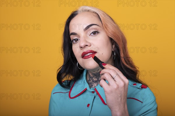Beautiful caucasian woman applying a bright red color lipstick on her lips over yellow background