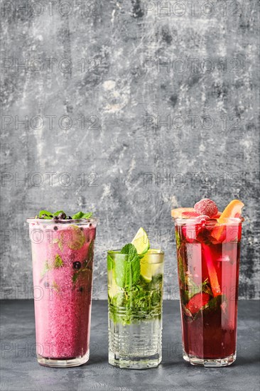 Three glasses with fruit refreshing drink on gray shabby background