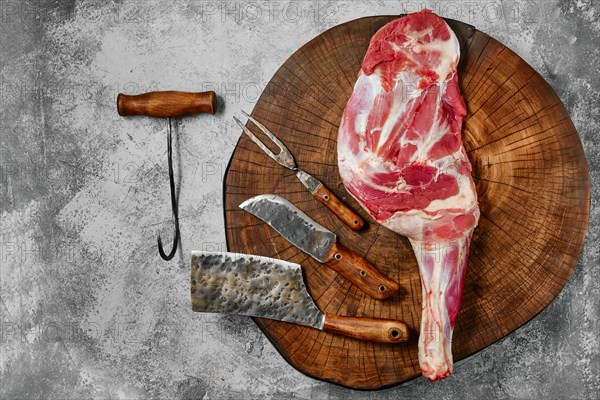Raw lamb shoulder chump on butcher's cutting log with tools