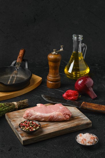 Raw veal steak bone in with ingredients for cooking on black background