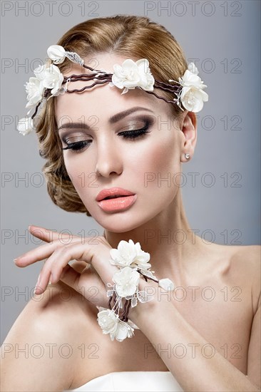 Portrait of a beautiful blonde woman in the image of the bride with flowers in her hair. Picture taken in the studio on a blue background