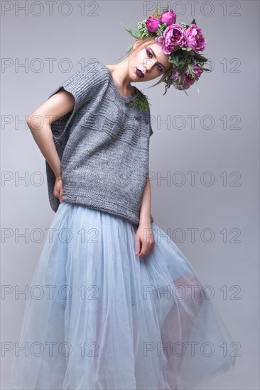 Beautiful girl with flowers on her head in fashion clothes posing against the background in the studio. Beauty Style