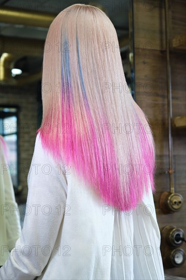 Beautiful blond girl with colored pink hair in a hairdressing salon. The client looks at herself in the mirror