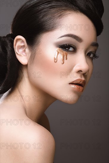 Beautiful girl with oriental type evening hair and makeup. Portrait shot in the studio on a gray background