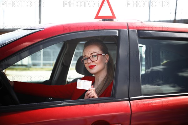 Joyful girl driving a training car with a drivers license card in her hands