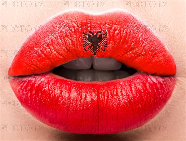 Female lips close up with a picture of the flag of Albania. Red and black emblem
