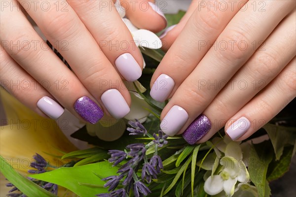 Purple neat manicure on female hands on a background of flowers. Nail design