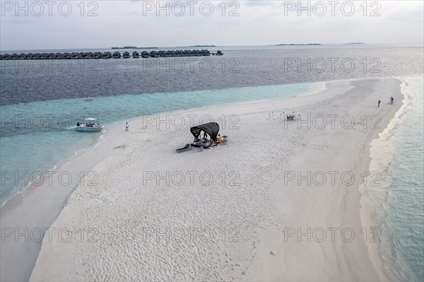 Aerial view: lonely sandbank in the Maldives with a table and sun loungers for romantic dinners