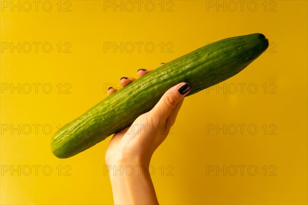Woman's hand with a vegetable on a yellow background
