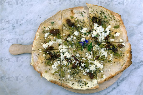 Flammkuchen with olives dried tomatoes and feta cheese on a wooden board