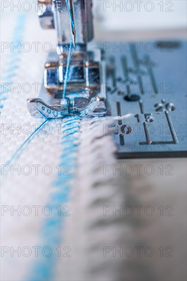 Close-up of sewing machine needle with blue thread sewing on a white fabric