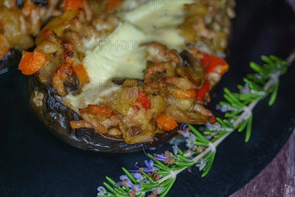 Foreground eggplant stuffed with meat and vegetables covered with bechamel sauce on a black slate on a wooden table
