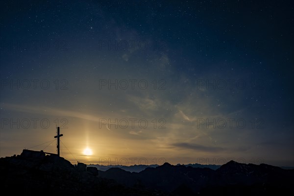 Summit cross of the Namloser Wetterspitze at full moon and Lechtaler Alps
