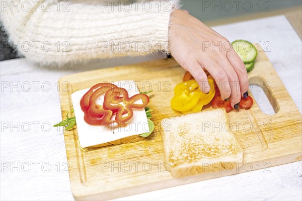 Unrecognizable person cooking a vegetable sandwich in the kitchen at home. Placing the red pepper