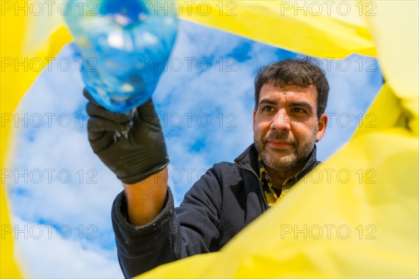 Man throwing a bottle into a garbage bag on the beach. Ecology
