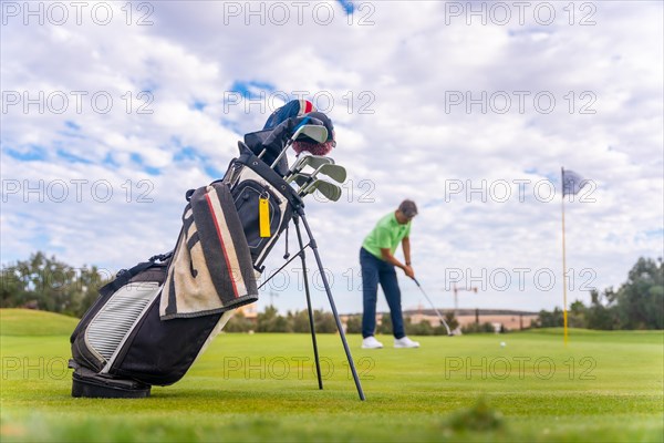 Caucasian professional golf player on the green preparing for the shot next to the fairway carrying bags