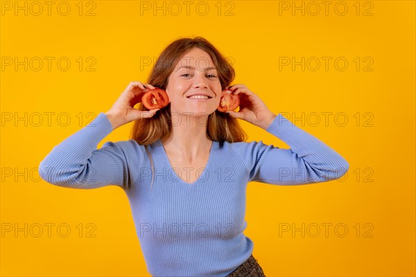 Vegan woman smiling with earrings tomato slices on a yellow background