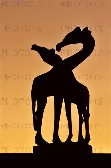 Wooden sculpture of African giraffes silhouetted against sunset