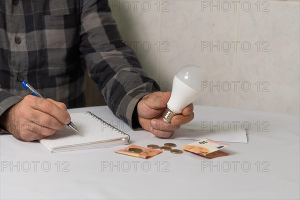 Man holding a light bulb writing down his expenses in a notebook