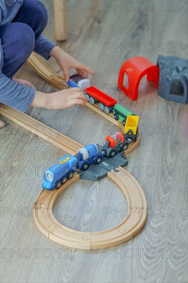 Unrecognizable child playing with a wooden train on the floor in his bedroom