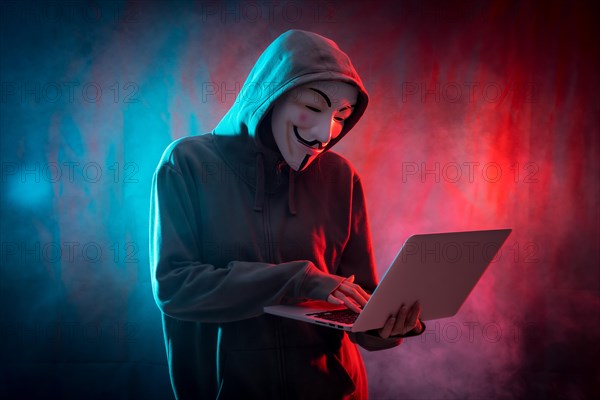 Hacker with anonymous mask with a computer and with a background of smoke and colored led