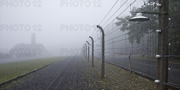 Reconstructed camp fence with crematorium in the fog at beech forest concentration camp