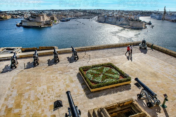 View over former parade ground with saluting cannons Battery Saluting Batter and flower bed in the form of Maltese Cross from historic Order of St. John next to Upper Barraka Garden on left Fort St. A...