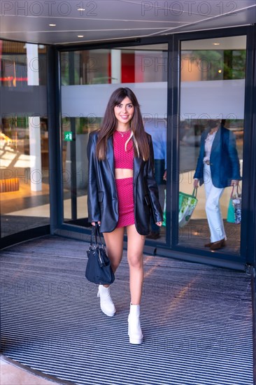 Portrait of a Caucasian girl in a red dress walking out of the revolving door of the shopping center