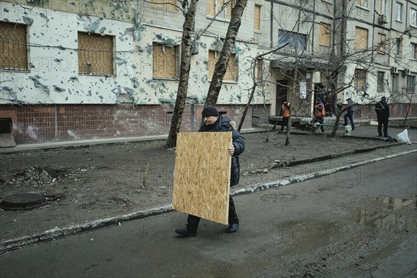 A man brings a chipboard to seal the destroyed windows