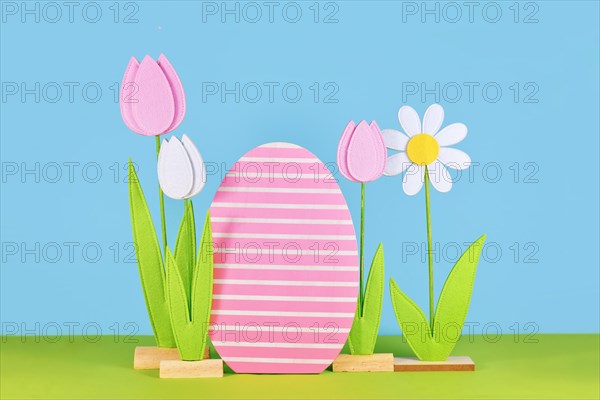 Easter arrangement with felt spring flowers and wooden easter egg in front of blue background