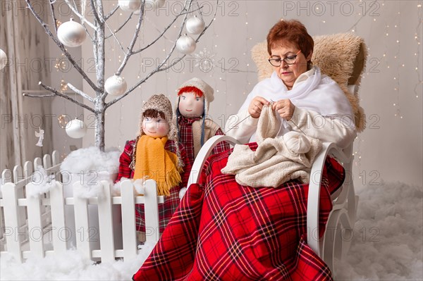A nice elderly woman sews to knit her granddaughters in a Christmas arrangement. In studio