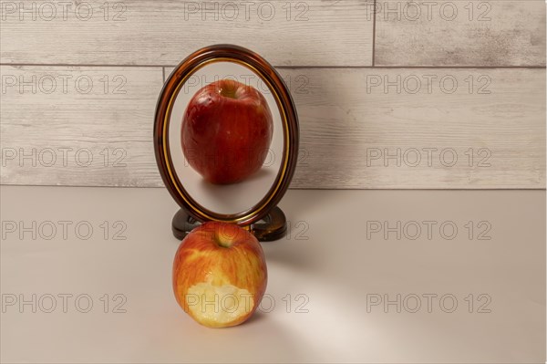 Bitten red apple reflected in a mirror isolated on a white table with copy space