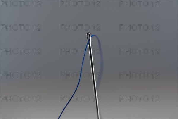 Sewing needle and blue thread against a neutral background