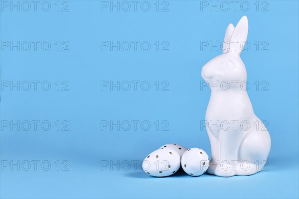 Easter bunny and white and gold Easter eggs with dots on blue background with copy space