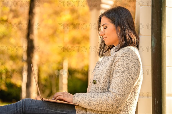 Pretty woman with glasses and MacBook in hand sits in the park at autumn time