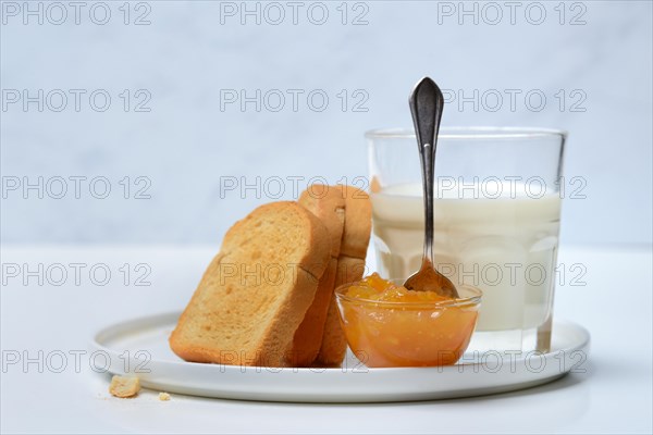 Rusk, glass of milk and orange marmalade in small bowls