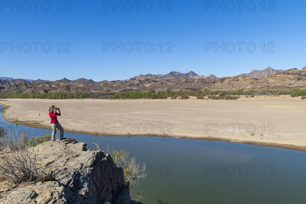 Woman taking pictures at the Orange River, also known as the Orange River, on the border between Namibia and South Africa, Oranjemund, Sperrgebiet National Park, also known as Tsau ÇKhaeb National Pa...
