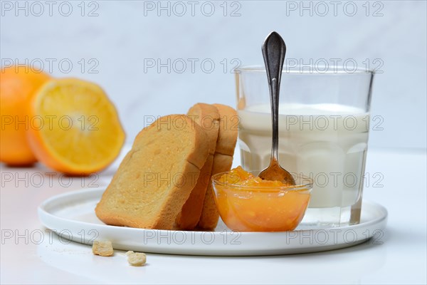 Rusk, glass of milk and orange marmalade in small bowls