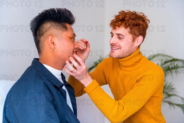 Beautiful gay couple putting on makeup painting their lips, being romantic indoors at home, lgbt concept