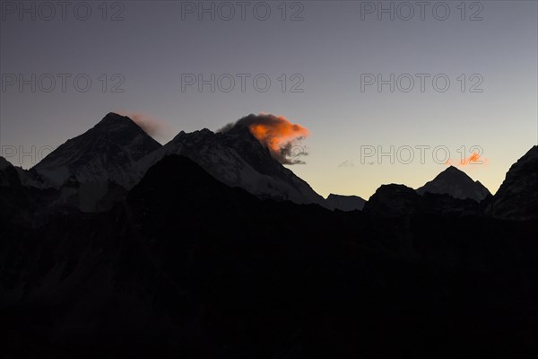 Daybreak at Gokyo Ri. Three clouds mark three eight-thousanders, Mount Everest on the left, Lhotse in the middle and Makalu on the right-hand-side in the greater distance. Silhouette of the mountain r...