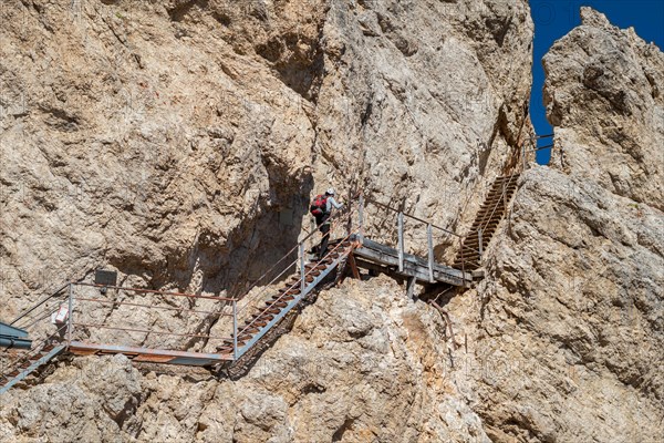 Tourist climbing steel stairs fixed to the rock. Dolomites