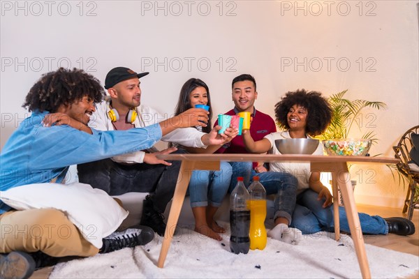 Group of friends eating popcorn and toasting with soft drinks. Laughing while watching a funny movie on TV at home