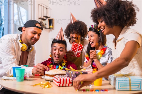 Multi-ethnic group of friends at a birthday party on the sofa at home with a cake and gifts