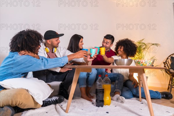 Group of friends eating popcorn and toasting with soft drinks. Laughing while watching a funny movie on TV at home