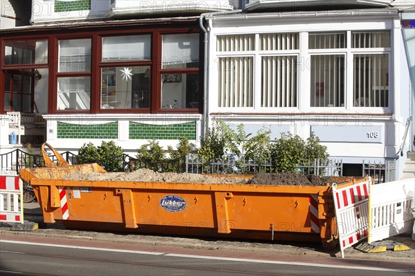 Orange skip for construction waste standing on the road in front of residential buildings
