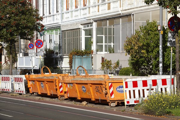 Orange skip for construction waste standing on the road in front of residential buildings
